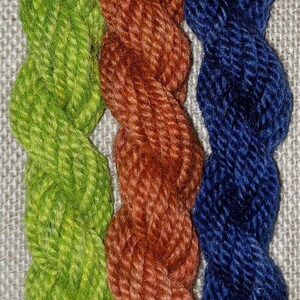 Könnte beinhalten: Drei Knäuel Garn in den Farben Grün, Orange und Blau. Das Garn ist gedreht und in einer vertikalen Reihe angeordnet.