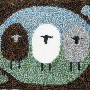 May include: A rug with a brown background and three sheep in the center. The sheep are brown, white, and gray. The sheep are standing on a green field with a blue sky above them.