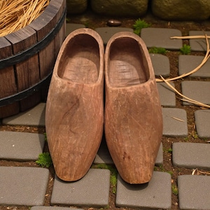 Peut inclure: Une paire de sabots en bois, présentant un fini grain de bois naturel. Les sabots sont de couleur marron moyen et reposent sur un chemin pavé. Ces chaussures traditionnelles sont de conception classique.