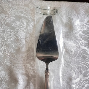 May include: A silver cake server with a decorative handle and the words "LUNT STERLING" printed on the packaging.