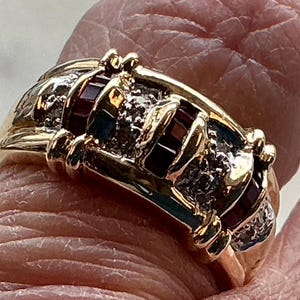 May include: A gold band ring with red and clear gemstones. The ring has a textured design and is set with multiple stones.