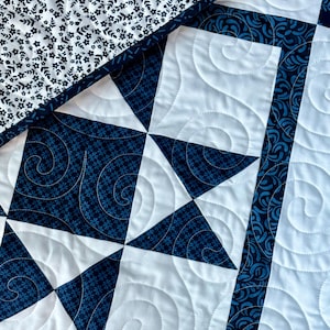 May include: Close-up of a handmade quilt with a patchwork design. The quilt features white and navy blue fabrics with floral and geometric patterns. The white sections have a spiral quilting pattern, and the edges are trimmed with a navy blue border.