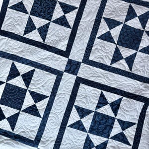 May include: A white and navy blue quilt with a star pattern. The quilt features large star blocks with navy blue star points and centers, framed by navy blue borders. The white background has a quilted swirl design.