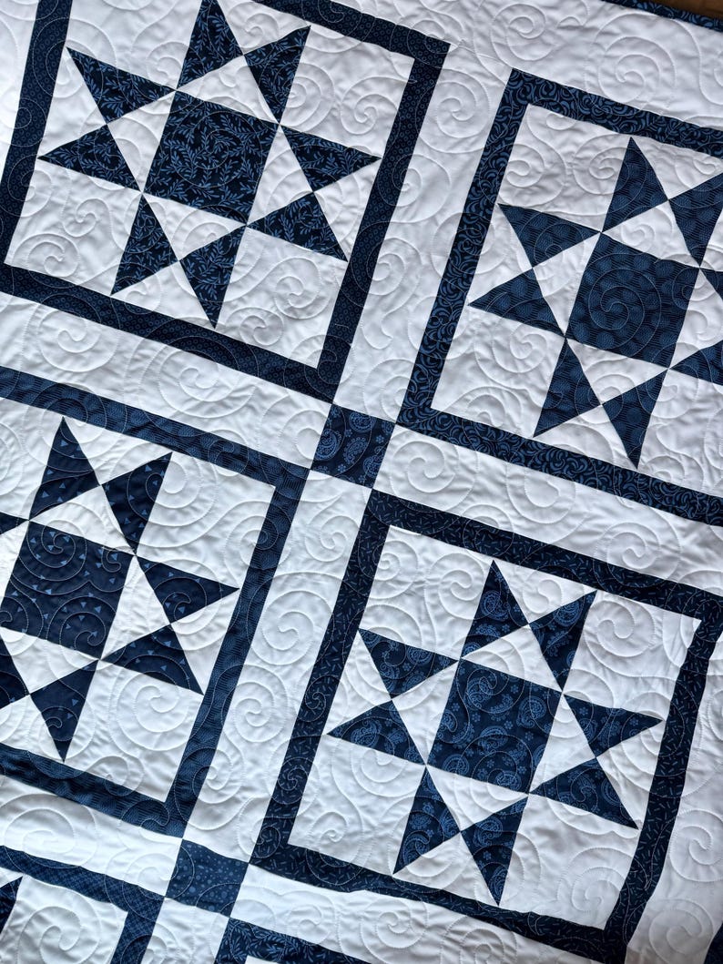 May include: A white and navy blue quilt with a star pattern. The quilt features large star blocks with navy blue star points and centers, framed by navy blue borders. The white background has a quilted swirl design.