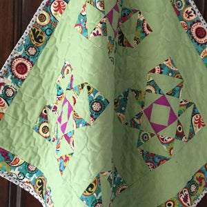 May include: A green baby quilt with a white border and a colorful paisley pattern. The quilt is made up of squares with a star design in the center.