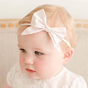 Puede incluir: Una diadema de satén blanco con lazo para bebés. La diadema está hecha de un material suave y elástico, perfecta para recién nacidos y niños pequeños.