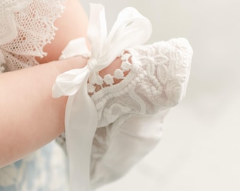 Könnte beinhalten: Weiße Spitzen-Babyschuhe mit einem weißen Satinband, das zu einer Schleife gebunden ist.