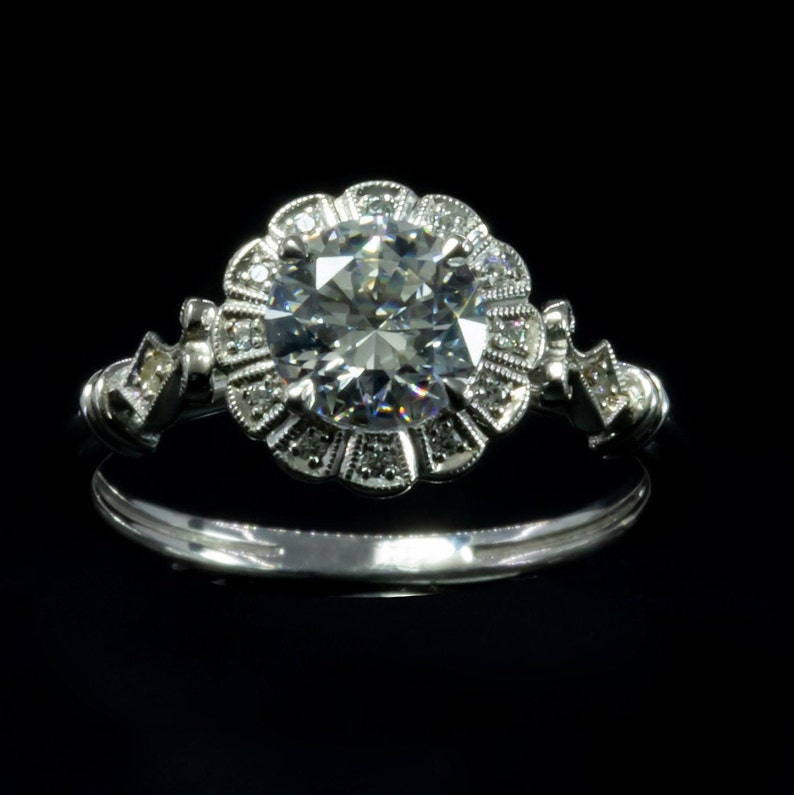 K&ouml;nnte beinhalten: Ein silberner Verlobungsring mit einem gro&szlig;en, runden, klaren Diamanten, der von kleineren Diamanten in einem floralen Design umgeben ist.
