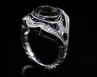 May include: A silver ring with a large, round, empty setting surrounded by a halo of smaller diamonds and blue sapphires.