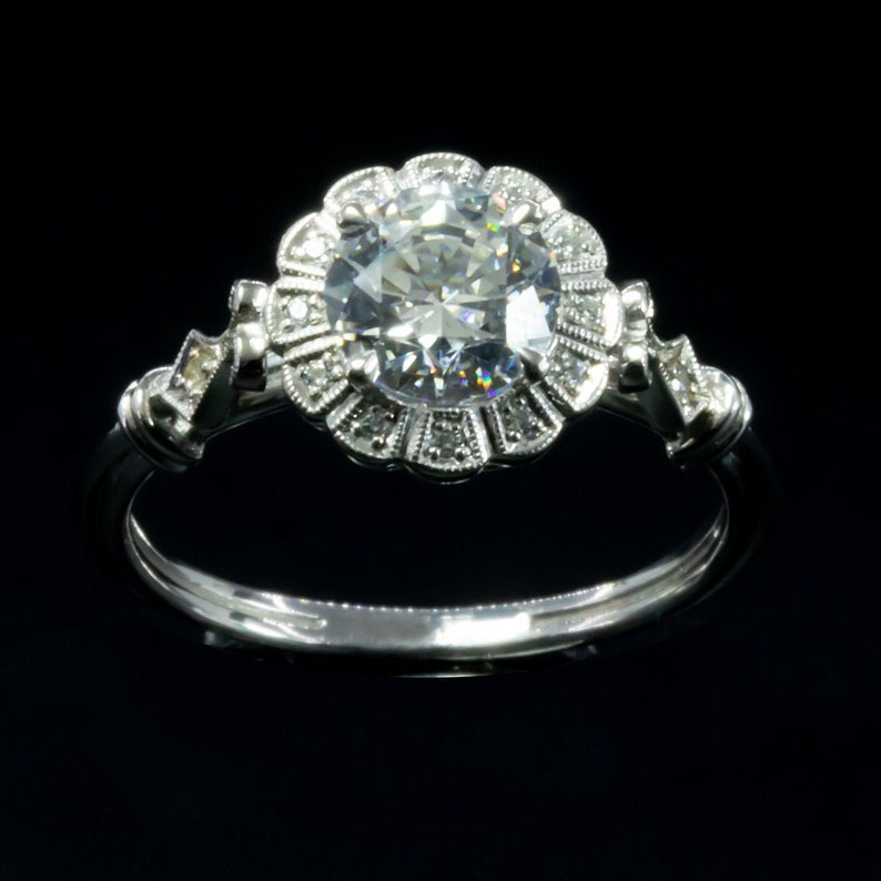 K&ouml;nnte beinhalten: Ein silberner Ring mit einem gro&szlig;en, runden, klaren Diamanten, der in einem floralen Heiligenschein-Design gefasst ist.