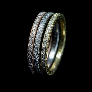 May include: Three gold, silver, and rose gold wedding bands with a row of small diamonds around each band.