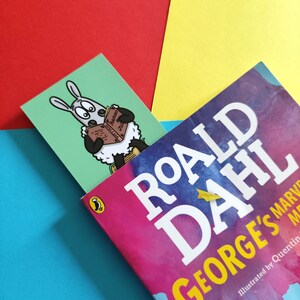 May include: A bookmark featuring a cartoon sheep reading a book titled "Baa-moo!" against a green background. The bookmark is placed on top of a book titled "Roald Dahl George's Marvellous Medicine" with a colourful watercolour design and a penguin logo.