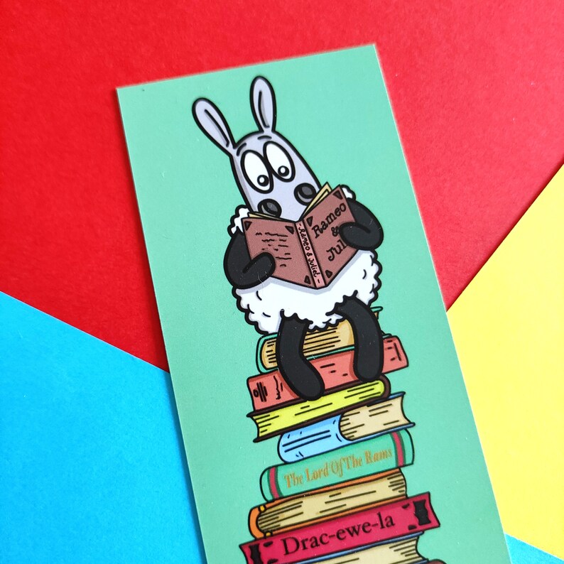 May include: A cartoon sheep wearing a black shirt sits on a stack of books. The sheep is reading a book titled "Rameo & Jul" and the other books are titled "The Lord Of The Rams" and "Drac-ewe-la".