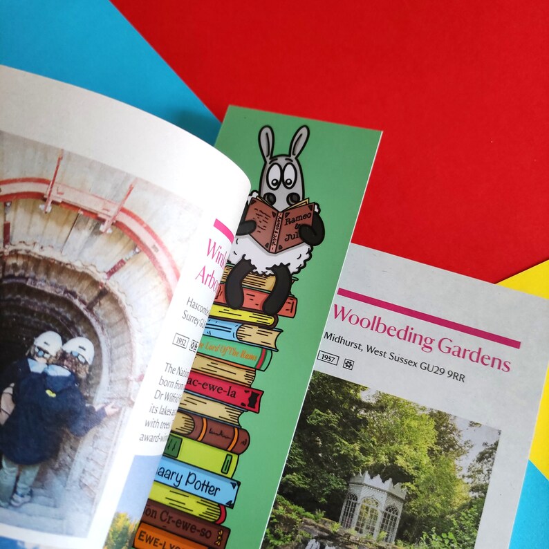 May include: A green bookmark featuring a cartoon sheep reading a book titled "Rameo Jul". The sheep is perched on a stack of books with titles including "The Lord of The Rings" and "Nac-ewe-la". The bookmark is alongside a brochure for Woolbeding Gardens in Midhurst, West Sussex, GU29 9RR.