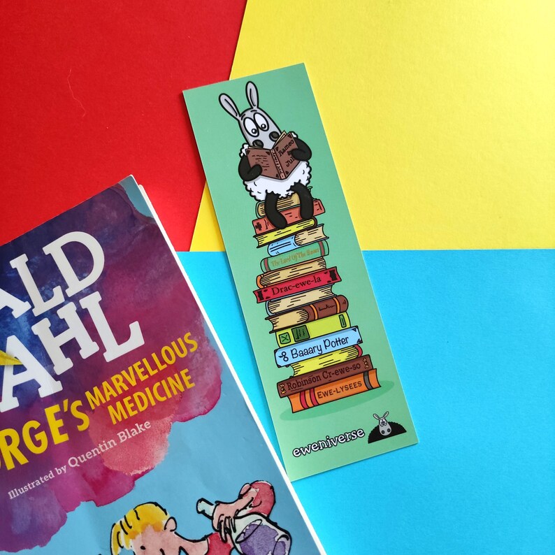 May include: A colourful bookmark featuring a cartoon sheep reading a book, standing on a stack of books with titles like "Drac-ewe-la" and "Baaary Potter". The bookmark has the text "eweniverse" at the bottom.