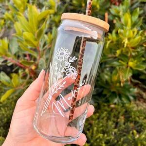 May include: A clear glass water bottle with a bamboo lid and a straw. The bottle has a floral design and the name "Malina" written on it.