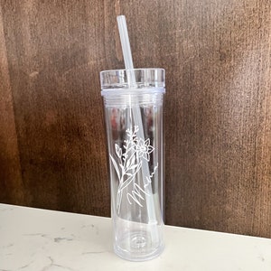 May include: Clear plastic tumbler with a straw and a floral design etched on the side. The design includes a flower and the word "Mama".