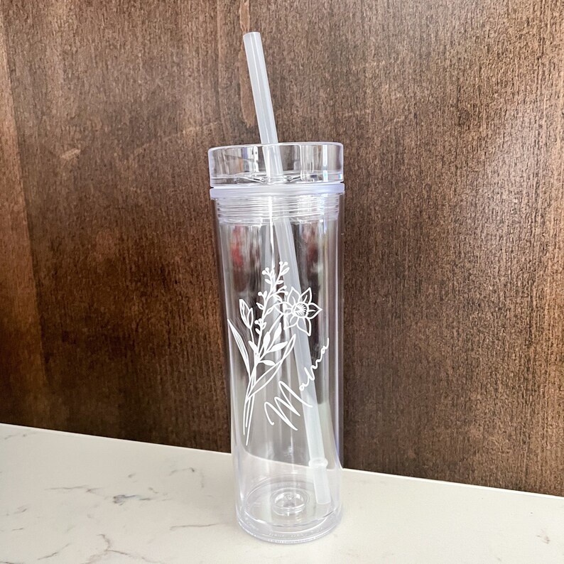 May include: Clear plastic tumbler with a straw and a floral design etched on the side. The design includes a flower and the word "Mama".