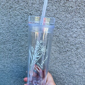 May include: Clear plastic tumbler with a white floral design and the word "Momma" written in cursive. The tumbler has a straw.