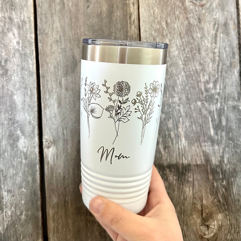 May include: White stainless steel tumbler with a floral design and the word "Mom" engraved on the side.