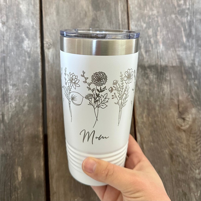 May include: White stainless steel tumbler with a floral design and the word "Mom" engraved on the side.