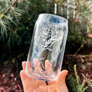 May include: A clear glass can with a white floral design and the name "Elizabeth" etched on the side.