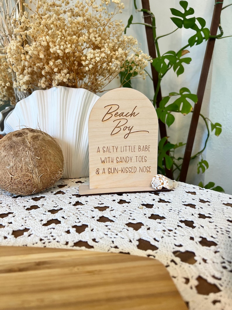 May include: Wooden sign with the text "Beach Boy" and the phrase "A salty little babe with sandy toes & a sun-kissed nose".