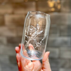 May include: A clear glass can with a floral design and the name "Andrea" etched into the side.