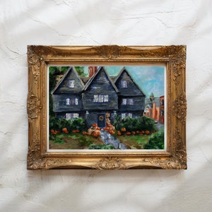May include: A painting of a dark gray house with a gold door and a wreath. The house is surrounded by a yard with pumpkins and trees. The painting is framed in a gold frame.