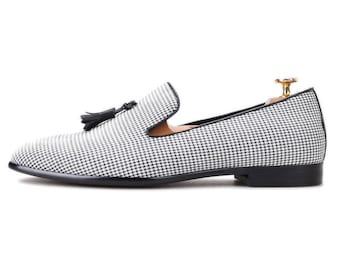 May include: A black and white houndstooth patterned loafer with a black tassel. The shoe has a black sole and a low heel. The shoe is designed for formal or semi-formal occasions.