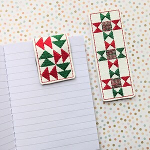 May include: Two fabric bookmarks with a geometric pattern of red, green, and white triangles. The bookmarks are on a white background with brown polka dots.