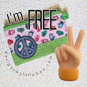 May include: A rectangular zipped pouch featuring a light pink fabric with a repeating pattern of colourful mittens and paw prints. The pouch has a green textured bottom panel, a green zip, and a circular blue denim patch with a peace sign symbol.