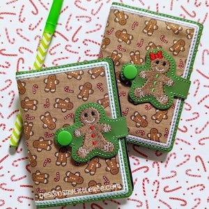 May include: Two small green and brown fabric covered notebooks with gingerbread man designs and a green button closure. The notebooks are on a white background with red and green candy cane designs.