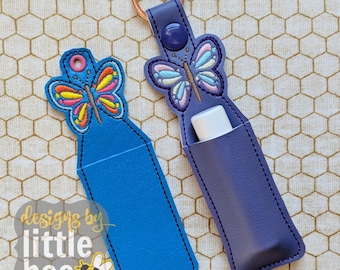 Puede incluir: Dos llaveros azules y morados con diseños de mariposas. Los llaveros están hechos de cuero y tienen un bolsillo para un bálsamo labial u otro artículo pequeño. El texto "designs by little bee" es visible en la esquina inferior izquierda de la imagen.
