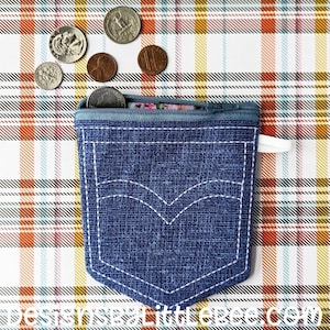 May include: A small blue denim coin purse with a zipper closure and a white stitched pocket detail. The purse is on a plaid fabric background with US coins scattered around it.