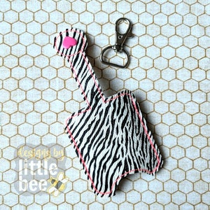 May include: A black and white zebra print hand sanitizer holder with a pink heart on the top. The holder has a silver key chain attached to it.