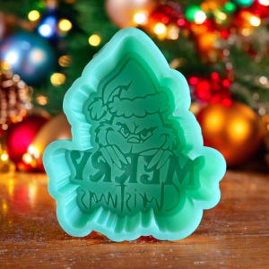 May include: Green silicone mold shaped like a Christmas tree with a Grinch character wearing a Santa hat and the text "Merry Christmas".