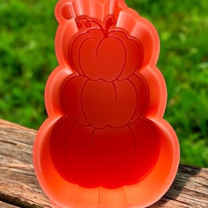 May include: A vibrant red, three-tiered pumpkin-shaped mold. The mold is made of a flexible material and features detailed pumpkin outlines. Perfect for creating festive treats for fall or Halloween.