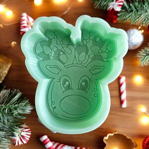May include: Green silicone mold shaped like a reindeer head with candy cane antlers and a string of lights. The mold is designed for making resin crafts.
