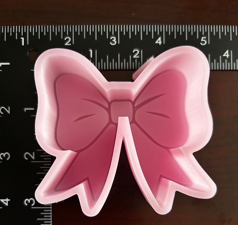 May include: Pink plastic cookie cutter shaped like a bow. The bow is about 2 inches wide.