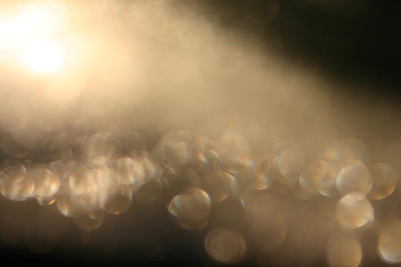 May include: An abstract image with a soft focus, displaying a gradient of warm, golden hues. The composition includes blurred, circular shapes creating a bokeh effect, suggesting light and depth. The overall aesthetic is dreamy and ethereal.