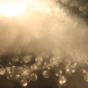 May include: An abstract image with a soft focus effect. The image shows a gradient of light and dark tones, with a scattering of out-of-focus, circular highlights. The overall colour palette is warm, with shades of gold and brown.