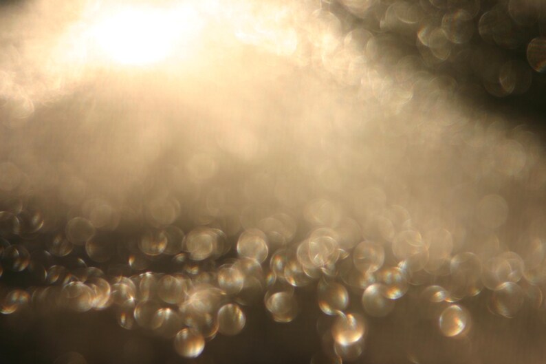 May include: An abstract image with a soft focus effect. The image shows a gradient of light and dark tones, with a scattering of out-of-focus, circular highlights. The overall colour palette is warm, with shades of gold and brown.