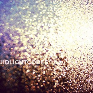 Op de afbeelding: Een close-up van een wazige, onscherpe afbeelding van een lichtbron die schijnt door een raam bedekt met waterdruppels. De druppels creëren een glinsterend, sprankelend effect, met een kleurverloop van paars naar goud.