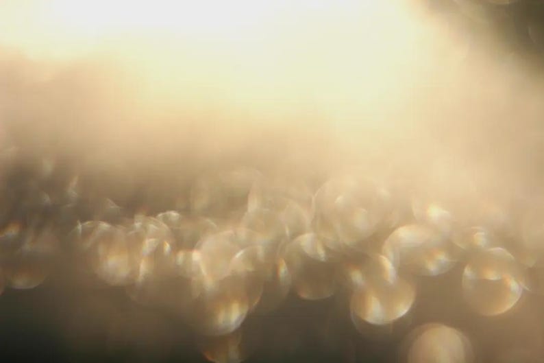 May include: An abstract image with a soft focus effect. The image shows a gradient of warm colours, shifting from a bright, light yellow at the top to a darker, muted gold at the bottom. The bokeh effect creates a dreamy, ethereal quality.