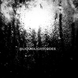 Puede incluir: Una fotografía en blanco y negro de una escena borrosa y fuera de foco, vista a través de una ventana cubierta de gotas de agua. El texto "@LIQUIDLIGHTCODES" es visible en el centro inferior de la imagen.