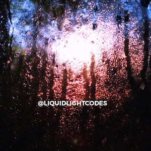 以下が含まれることがあります： 窓から見た夕焼けのぼやけた画像で、窓ガラスに雨滴がついています。画像の下中央に「@LIQUIDLIGHTCODES」というテキストが表示されています。
