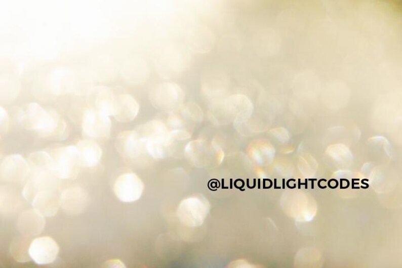 K&ouml;nnte beinhalten: Abstraktes Bild mit Weichzeichner-Effekt, das einen Bokeh-Effekt aus schimmernden, unscharfen Lichtern in Gold- und Wei&szlig;t&ouml;nen zeigt. Der Text "@LIQUIDLIGHTCODES" ist in Schwarz dargestellt.