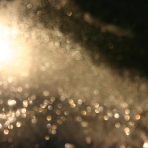 May include: An abstract image featuring a bright, blurred light source and bokeh effects. The light source is a bright white, with gold and white bokeh, creating a dreamy, ethereal effect. The image has a soft, out-of-focus quality.