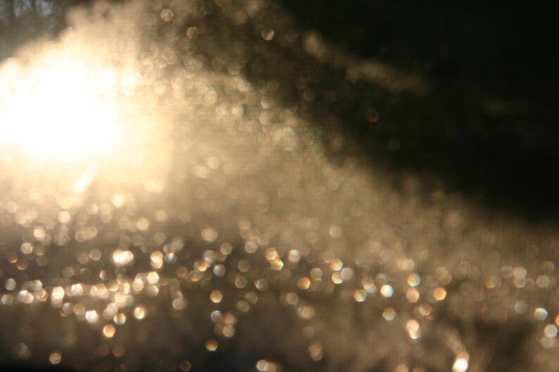 May include: An abstract image featuring a bright, blurred light source and bokeh effects. The light source is a bright white, with gold and white bokeh, creating a dreamy, ethereal effect. The image has a soft, out-of-focus quality.